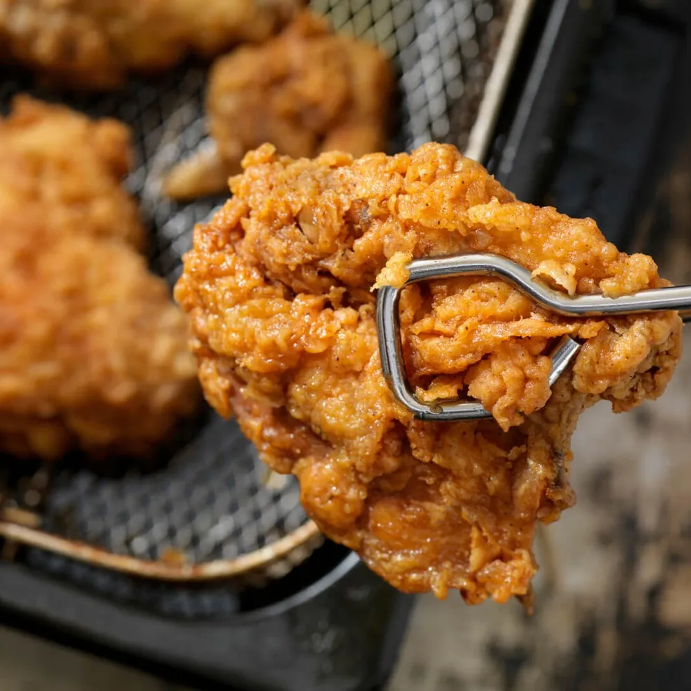 Fried chicken piece removed from fryer with tongs