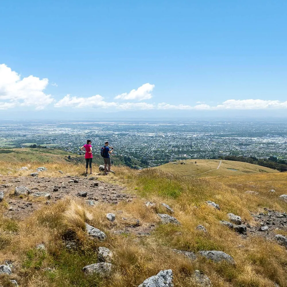 Two people standing on top of the Port Hills with Christchurch city in the background.