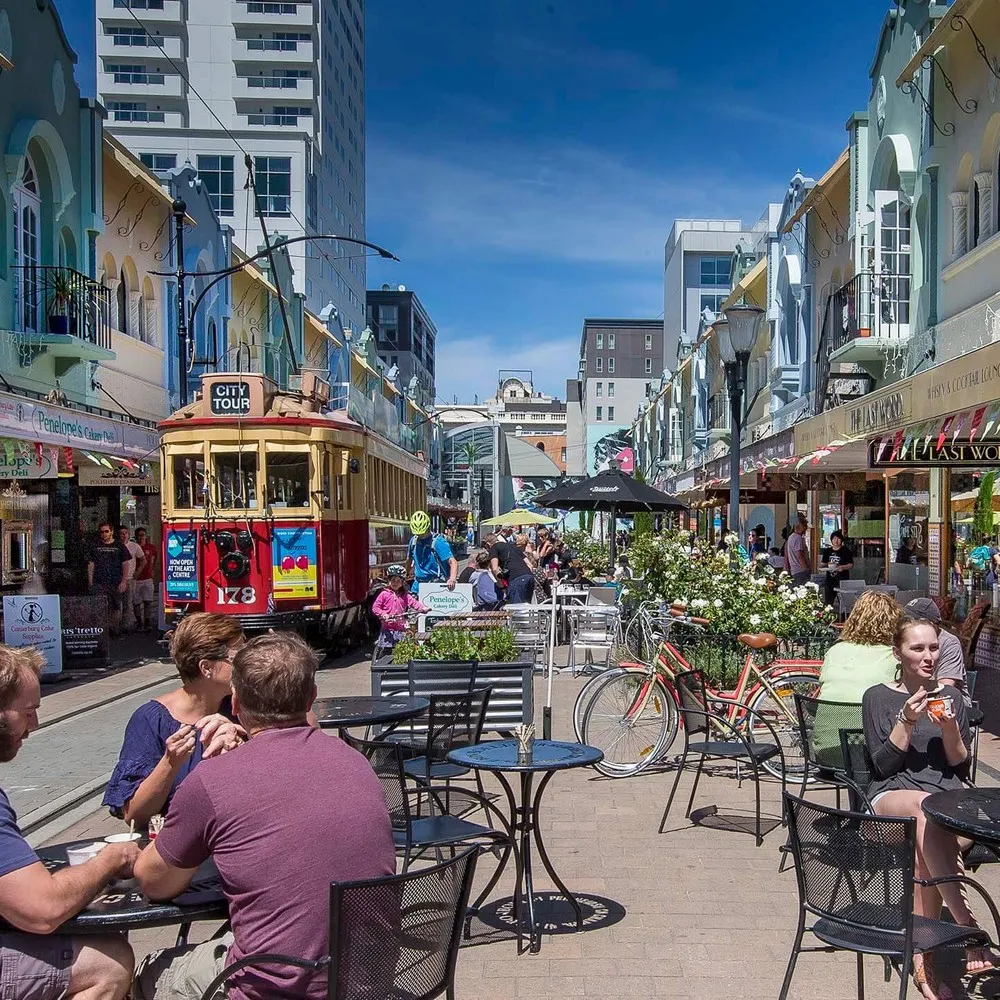 Tram moving down New Regent Street with lots of people sitting outside cafes enjoying coffee.