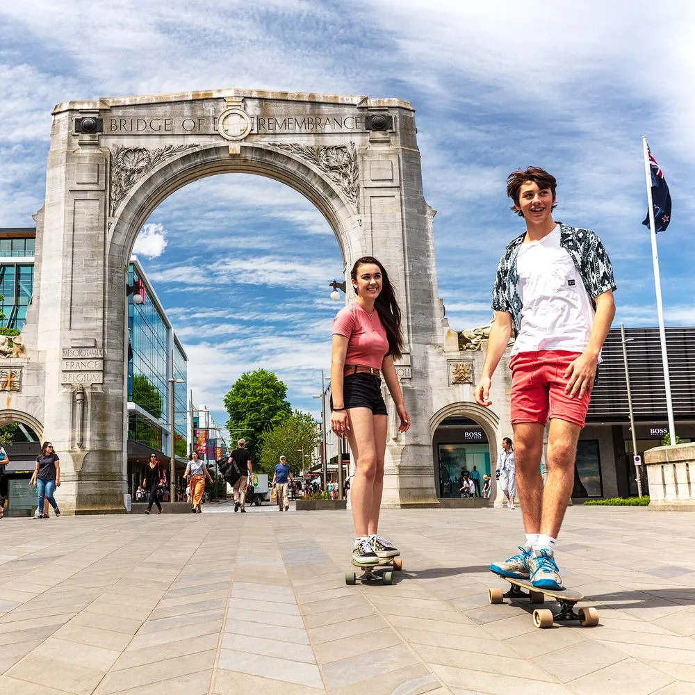 Two students skateboarding in front of the Bridge Of Remembrance.