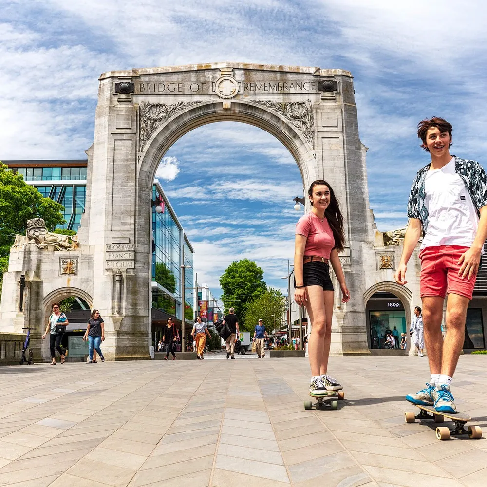 Two students skateboarding in front of the Bridge Of Remembrance.