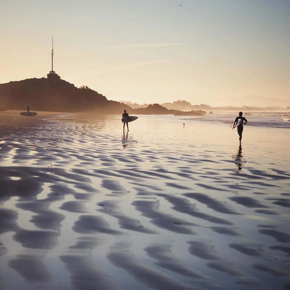 People walking on Scarborough Beach with surfboards, Cave Rock in the background.
