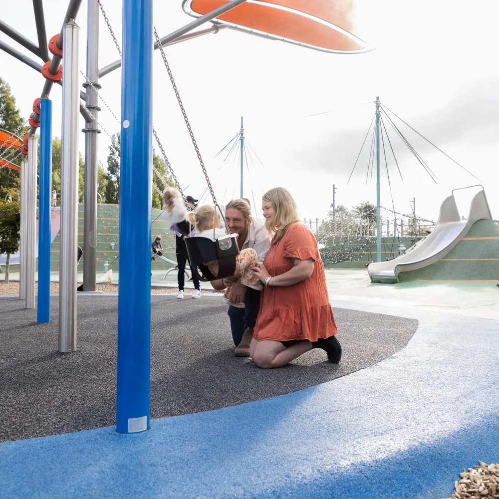 Family pushing child on a swing at the Margaret Mahy Playgound.
