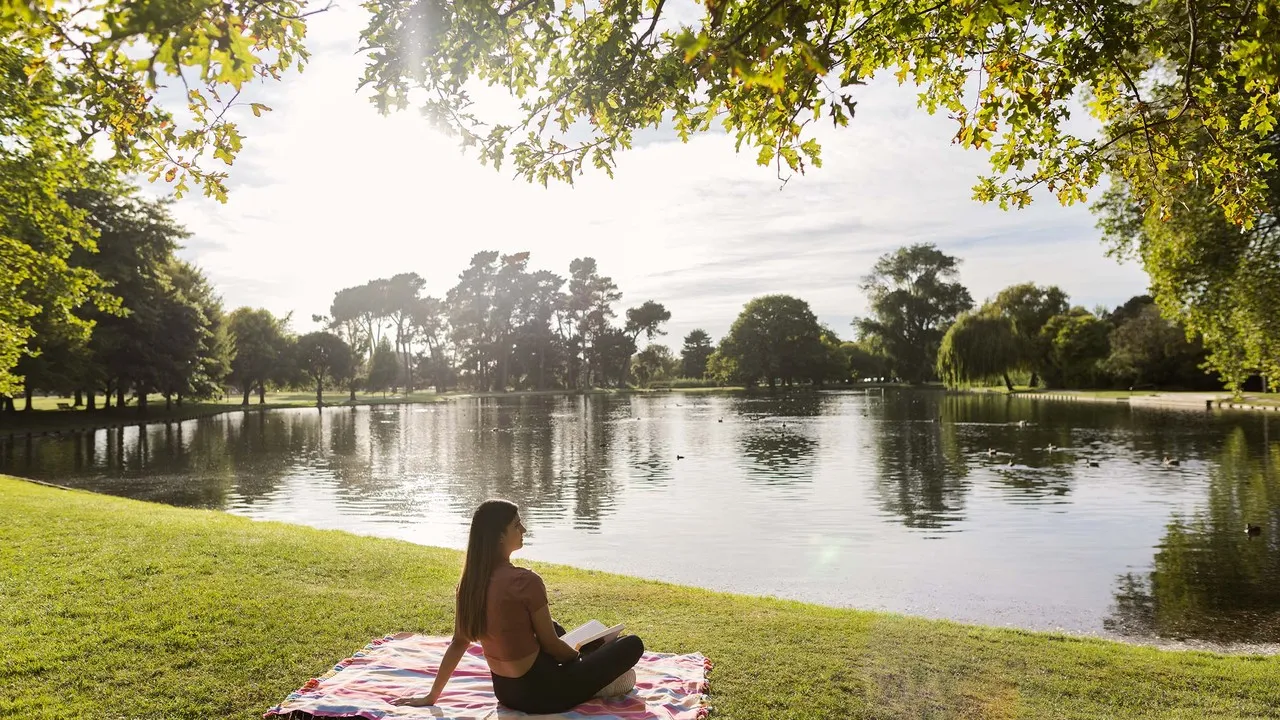 Lady taking time out to relax and read a book by the lake in Hagley Park.