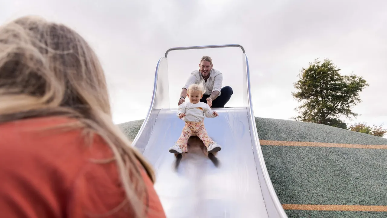 Child on slide and family enjoying Margaret Mahy Playground.