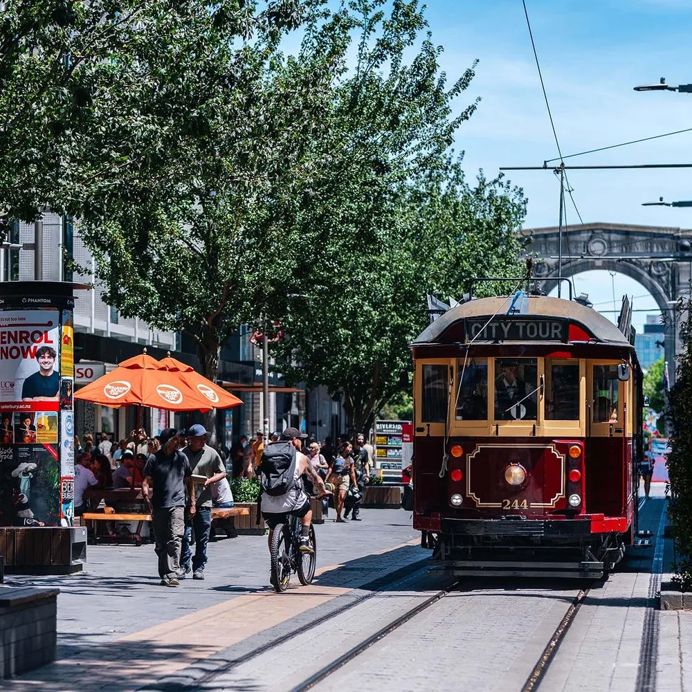 Red Tram driving down city mall with Bridge of Remembrance in the background.