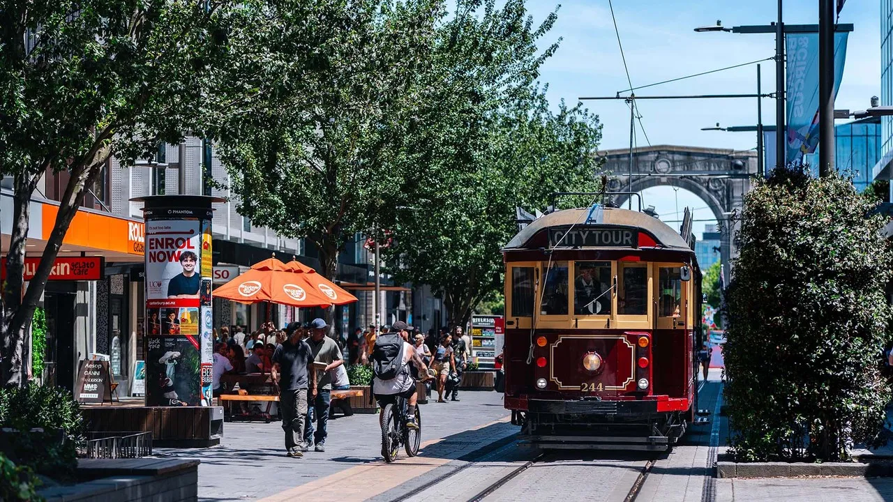 Red Tram driving down city mall with Bridge of Remembrance in the background.