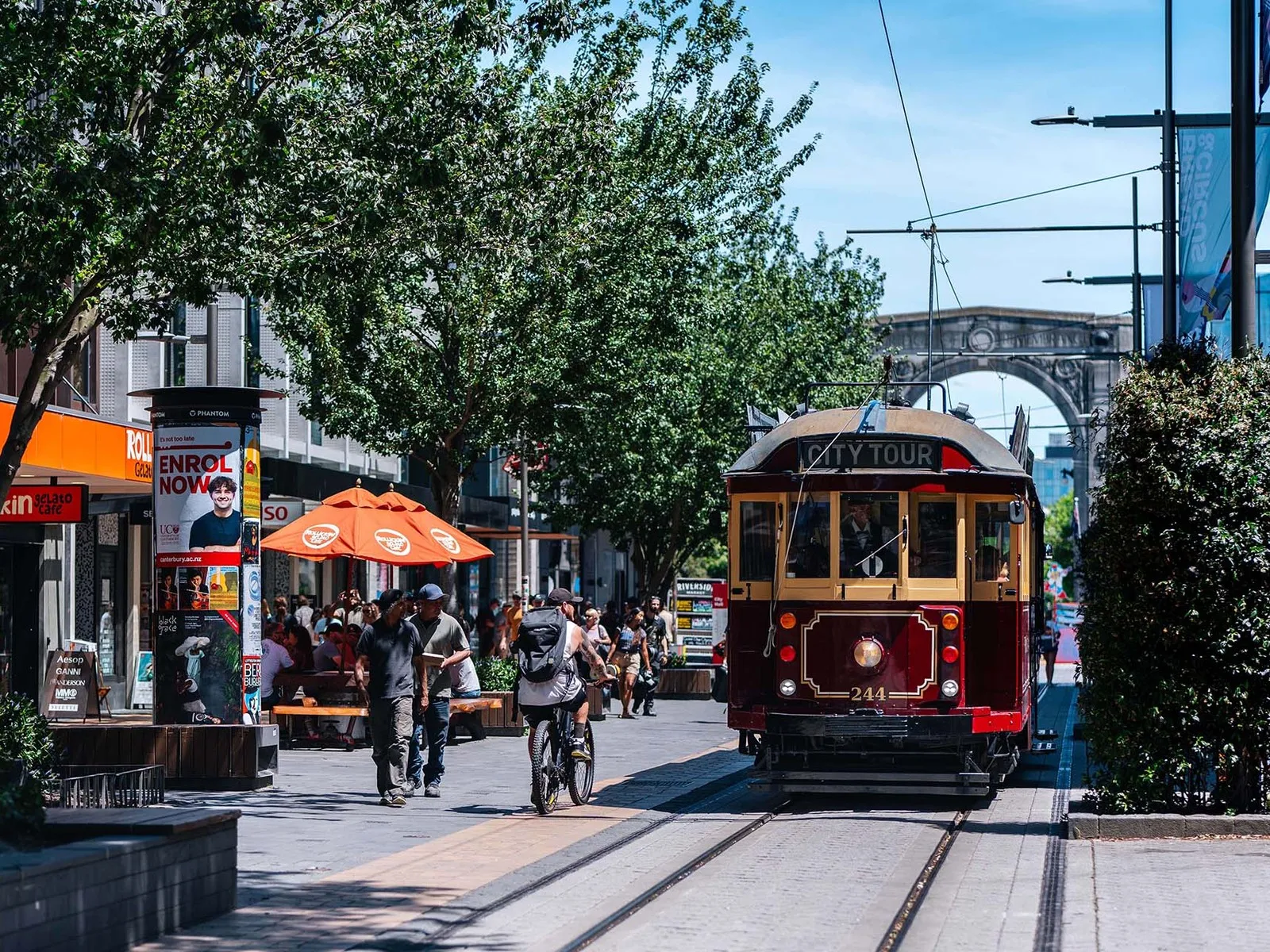 Red Tram driving down city mall with Bridge of Remembrance in the background.