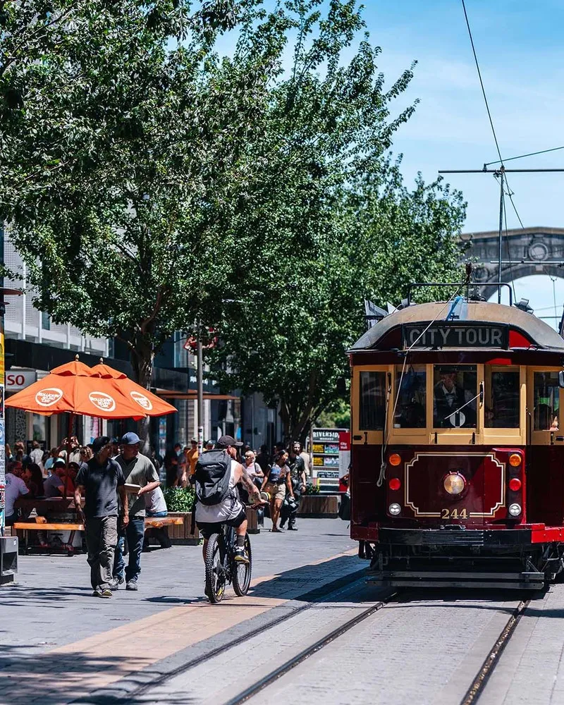 Red Tram driving down city mall with Bridge of Remembrance in the background.