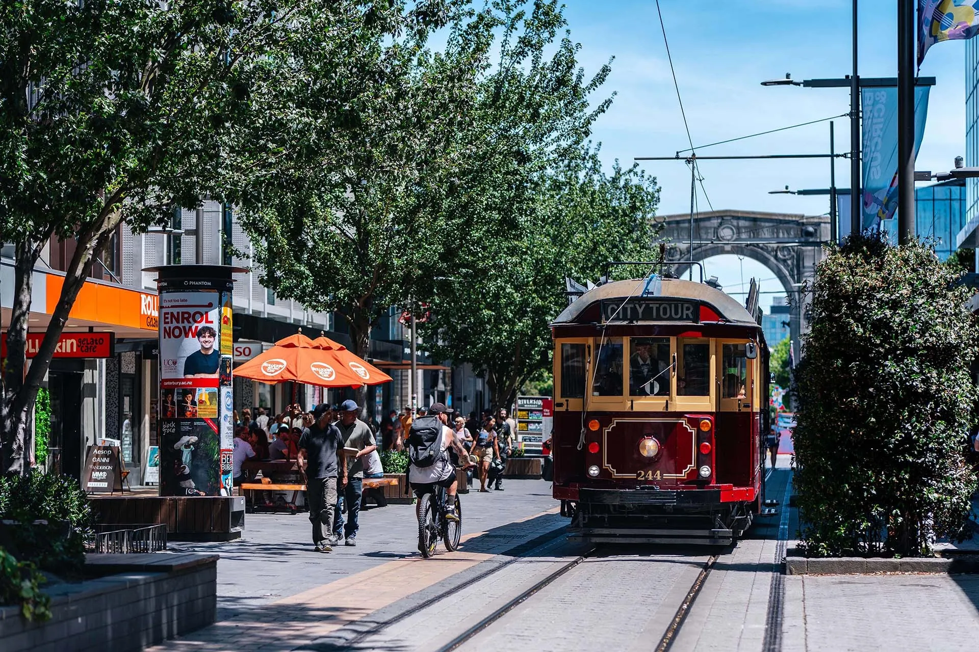 Red Tram driving down city mall with Bridge of Remembrance in the background.