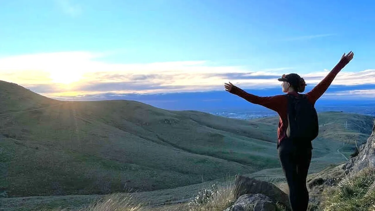 Influencer Laura Waddell standing on the Port Hills facing the sun with her arms in the air