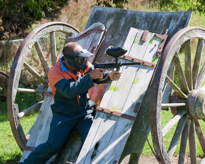 Paintball game in action, participant uses a upturned cart for cover