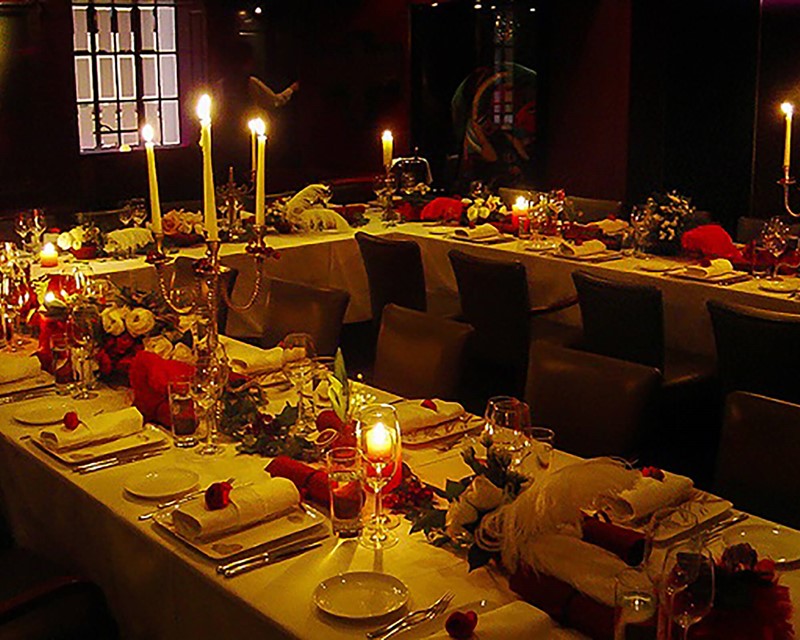 Trestle tables set in a U shape, with candelabras red and white feathers lay on the table
