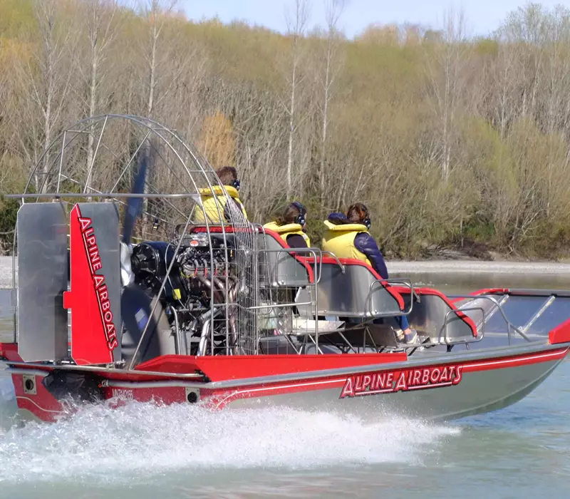 Close up of the airboat in action, the red and silver boat holds three passengers with rain jackets and yellow life jackets 