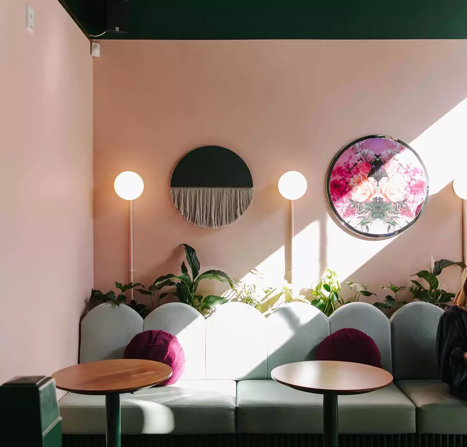 Interior of gin gin, pink wall and mint couches. Lady enjoy a wine at the table.