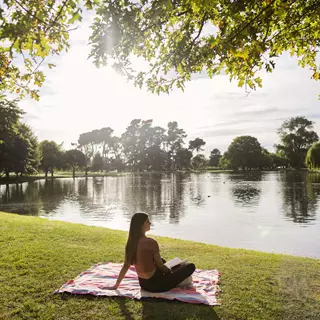 Lady Sitting On Blanket By Lake Relaxing At Hagley Park