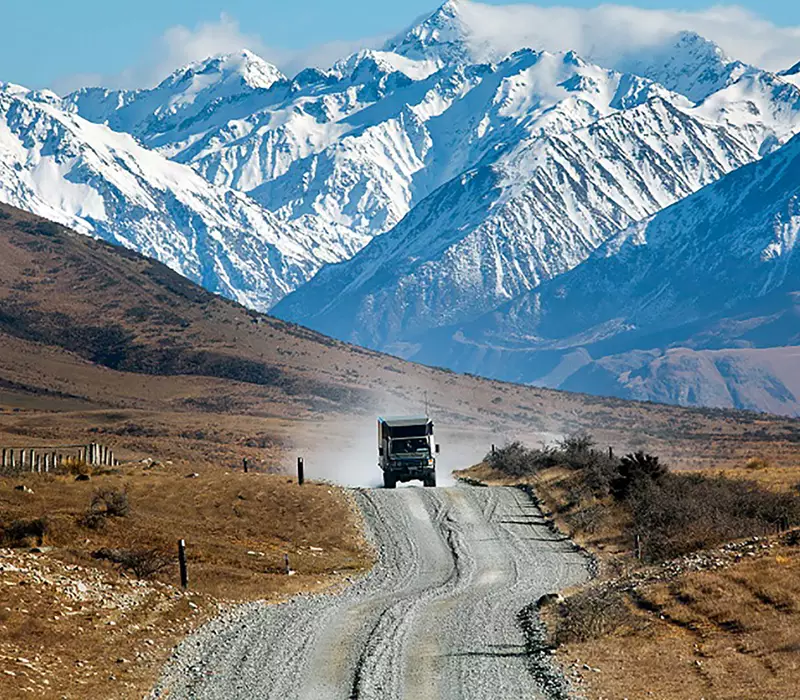 Hassle Free Tour van travels along a gravel round with snowy mountains in the background