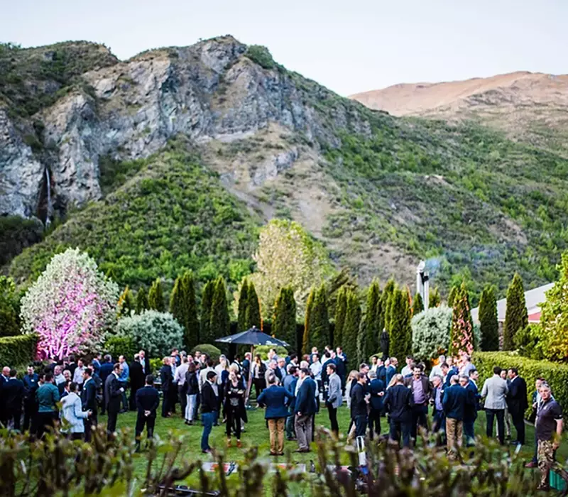 An outside cocktail event in lush green, manicured gardens. In the background dramatic rocky cliff faces create a strong backdrop 