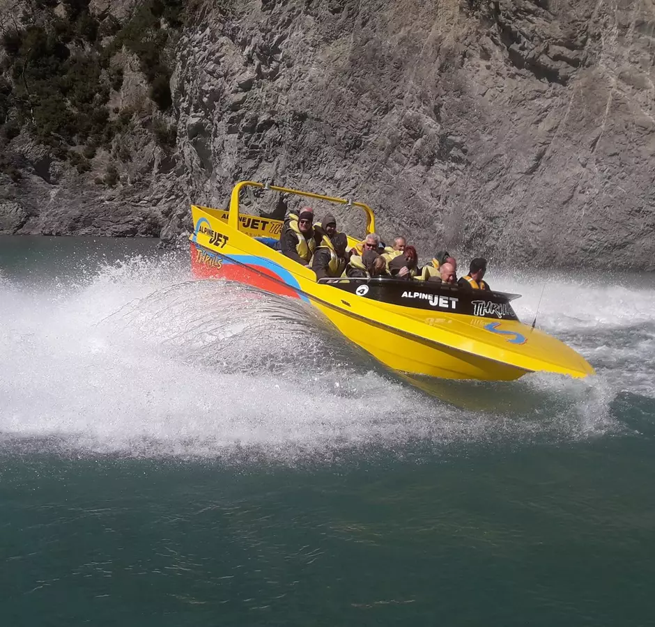 The yellow and orange jet boat is mid spin, white water breaks around it. 