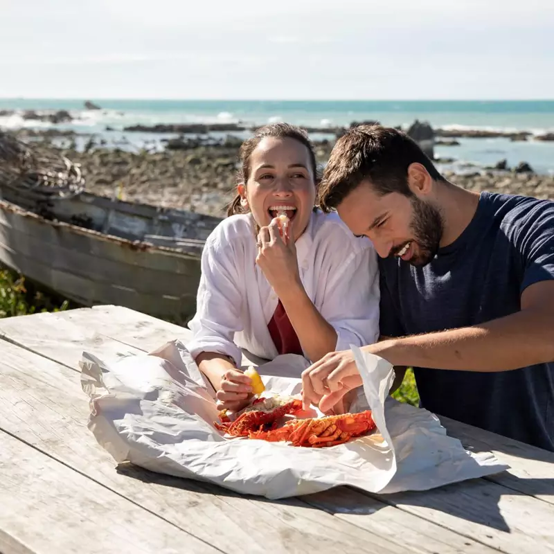 A couple in Kaikoura eating crayfish with squeezed lemon on the shore.