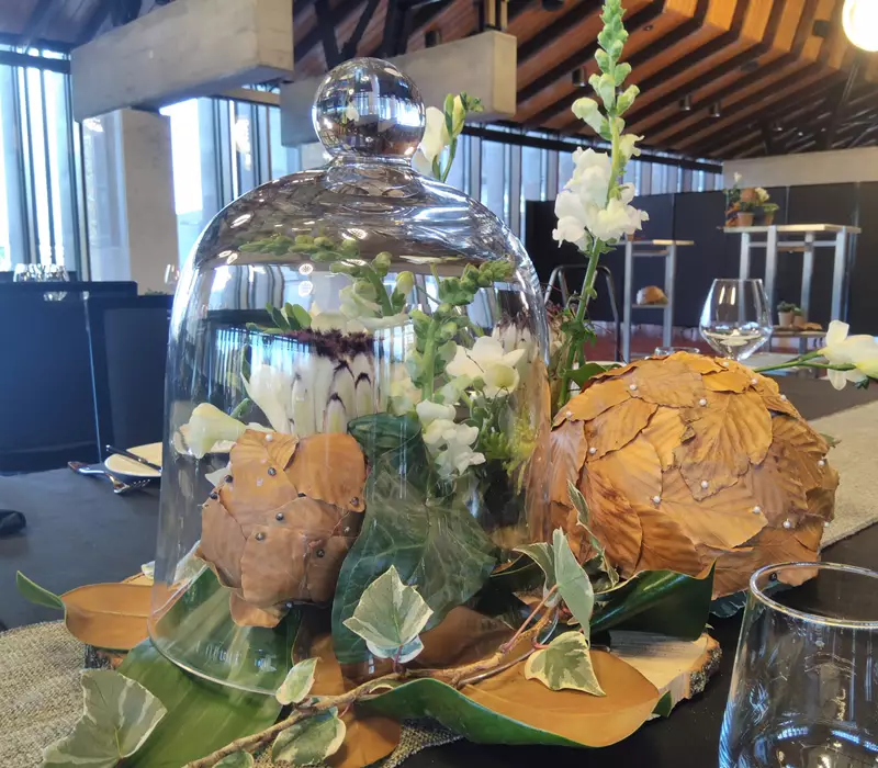 Table centerpiece, large green and brown leaves with flowers and glass dome over the top  