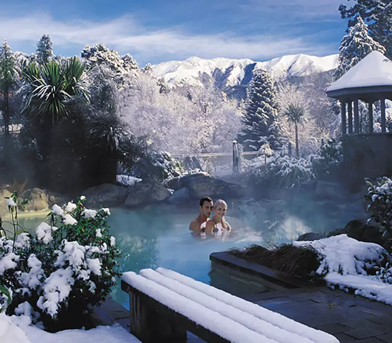 A couple relax in the thermal pools in winter, snow lines the pools