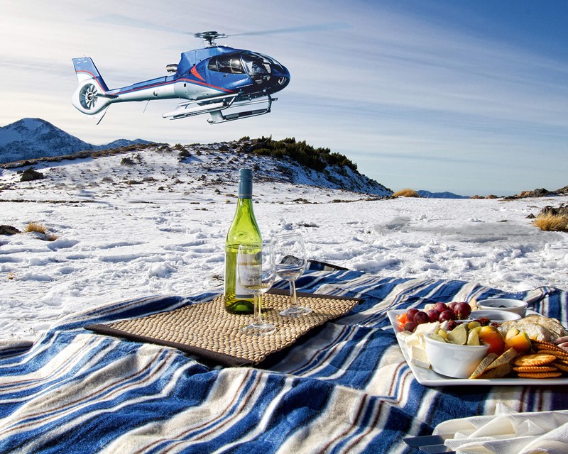 A helicopter lands near where a picnic has been set up in the snow