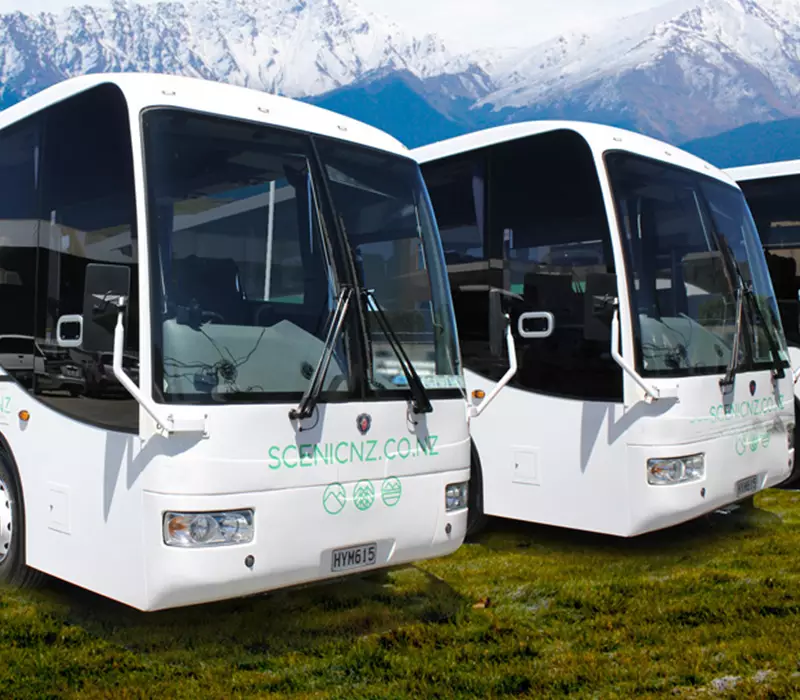 three buses line side by side in front of mountain ranges